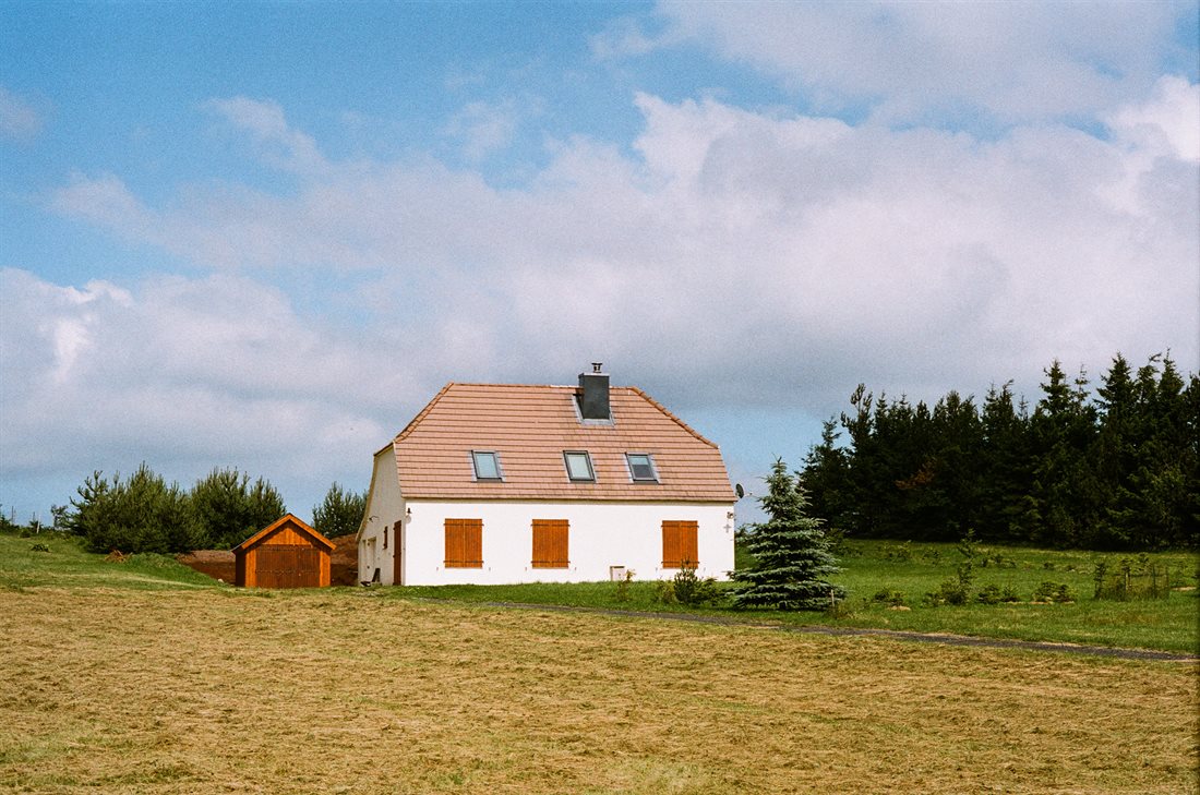 Ardèche, grande maison isolée au milieu d'un immense champ vert et jaune, cabanon, volets fermées, ciel bleu nuages lumineux 